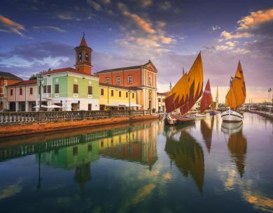 Colorful buildings and sailboats reflected in the canal water.