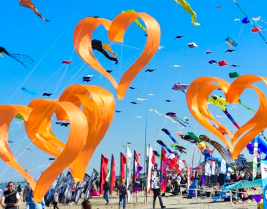 Festival di aquiloni con cuori arancioni in cielo, giornata soleggiata.