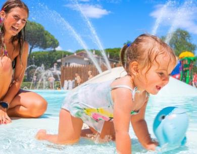 Bambina gioca in piscina con la mamma, giornata soleggiata.