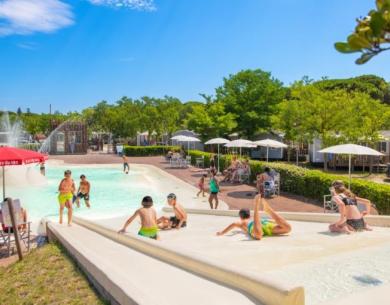 Piscina con scivoli, bambini giocano sotto il sole estivo.