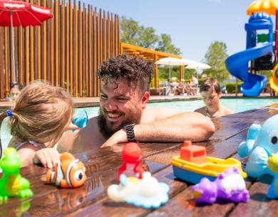 Papà e figlia giocano in piscina con giocattoli colorati.