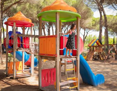 Bambina gioca nel parco giochi colorato tra gli alberi.