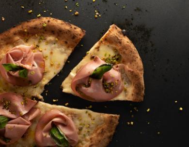 Pizza con mortadella, pistacchi e basilico su sfondo scuro.