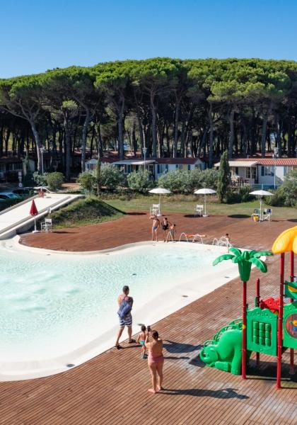 Outdoor pool with slides and children's play area, surrounded by pine forest.