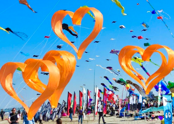 Festival di aquiloni con cuori arancioni in cielo, giornata soleggiata.