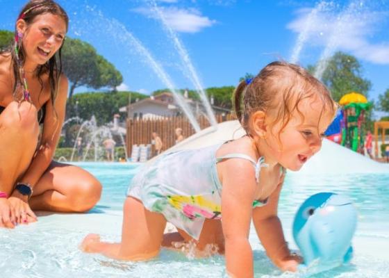 Bambina gioca in piscina con la mamma, giornata soleggiata.