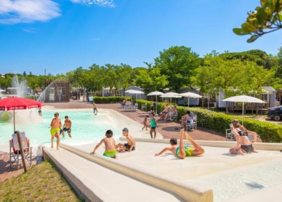 Piscina con scivoli, bambini giocano sotto il sole estivo.