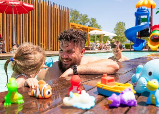 Papà e figlia giocano in piscina con giocattoli colorati.