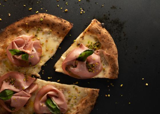 Pizza con mortadella, pistacchi e basilico su sfondo scuro.